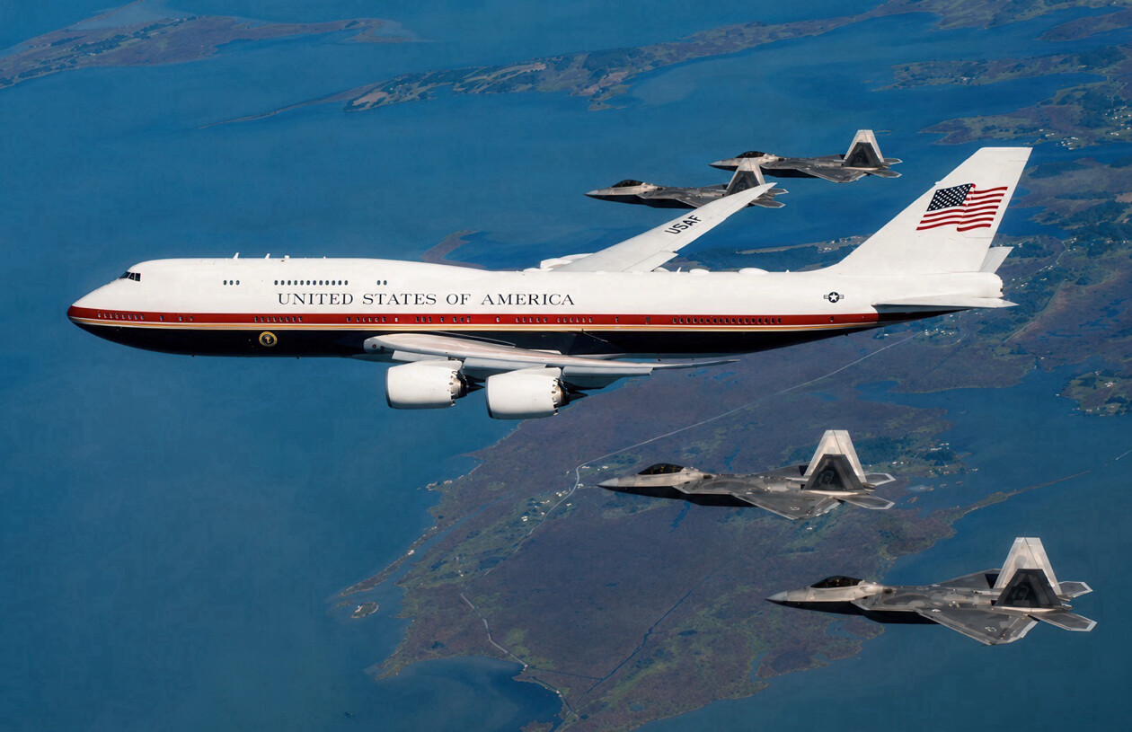 The U.S. presidential-configuration Boeing 747 is escorted by four F-22 Raptor fighter jets above a coastal region on 07/12/2026.